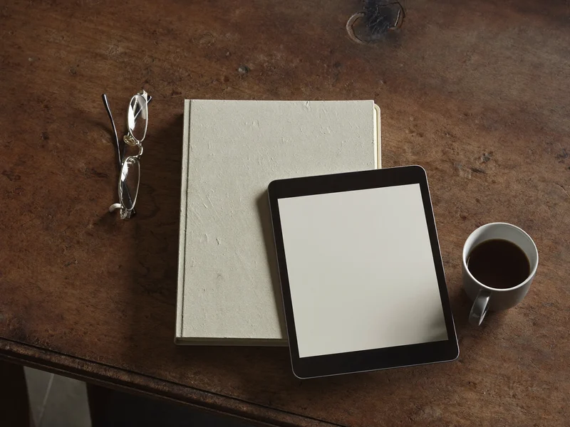 Quaderno, occhiali, caffè e tablet su un tavolo di legno consumato